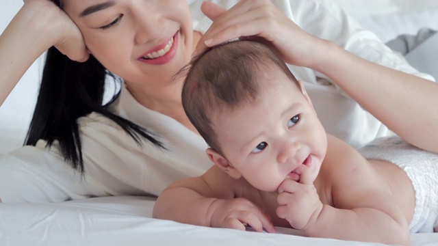 妈妈和她的孩子在卧室里玩。快乐幸福的家庭。家庭关系，亚洲家庭，新生儿，人寿保险。关系与人、儿童、童年与亲子观念。东南亚和东亚:亚洲婴儿视频素材