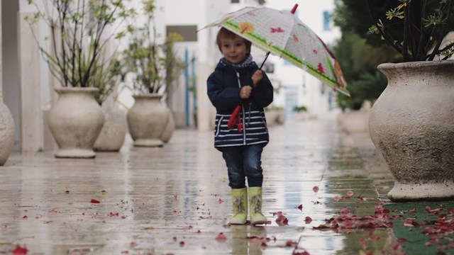 一个穿着胶靴的孩子在雨中拿着喇叭走着视频素材