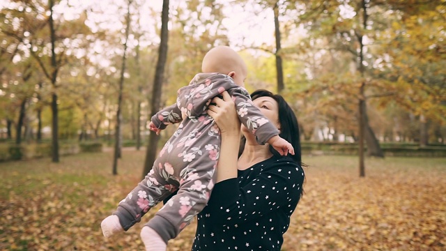 年轻的妈妈带着漂亮的宝宝在秋天的公园里，慢镜头。视频素材