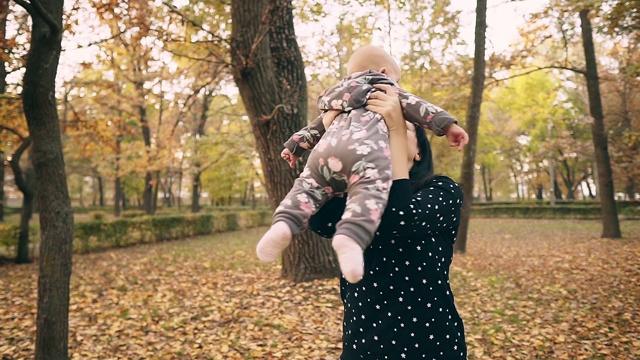 年轻的妈妈带着漂亮的宝宝在秋天的公园里，慢镜头。视频素材