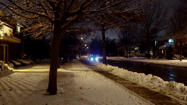 汽车行驶缓慢，在积雪覆盖的居民区街道上，夜间车灯自然在冬夜穿行视频素材