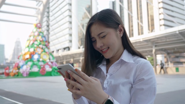 兴奋的商业亚洲女人庆祝好消息检查智能手机在曼谷晚上的现代城市中心泰国。技术沟通，成功靠手机视频素材