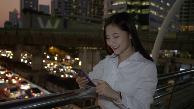 兴奋的商业亚洲妇女庆祝好消息检查智能手机在现代城市中心在泰国曼谷晚上。技术沟通，成功靠手机视频素材