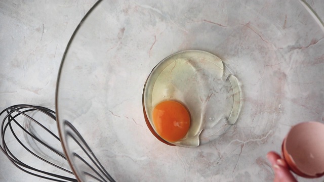 用手在玻璃碗中敲碎鸡蛋，俯视图。自制的烹饪视频素材