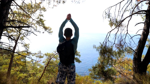 男性徒步旅行者背包来到边缘山，欣赏美丽的海景。享受旅行的人表现出快乐的情绪或幸福。游客在旅行中积极休息，享受自由。视频素材