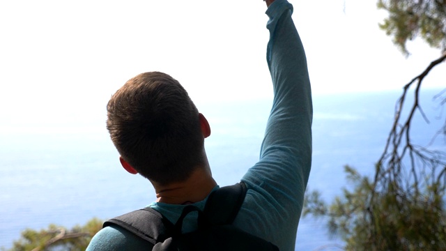 背包男徒步者站在山腰欣赏美丽的海景。享受旅行的人表现出快乐的情绪或幸福。游客在旅行中积极休息，享受自由。视频素材