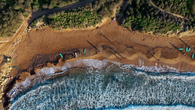 Ghajn Tuffieha海滩鸟瞰图。冲浪者。日落，青山绿水，沙滩，海浪在海里。冬天。相机的静态的。马耳他视频素材