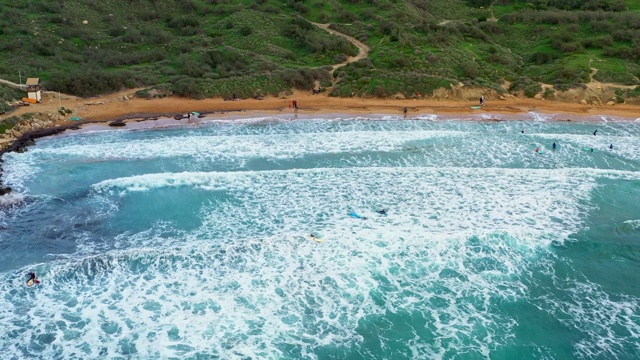 在Ghajn Tuffieha海滩上的冲浪者。日落，青山绿水，沙滩，海浪在海里。冬天。马耳他岛视频素材