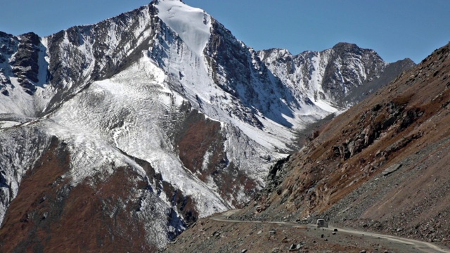 长焦镜头拍摄的白色4x4驾驶在砾石道路通过崎岖的地形和白雪覆盖的雄伟山脉。视频素材