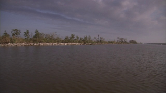 小波浪沿着一条长棕色的河边荡漾，河两旁种着树。视频素材