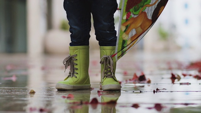 雨中穿着胶靴的小男孩站在水坑里视频素材