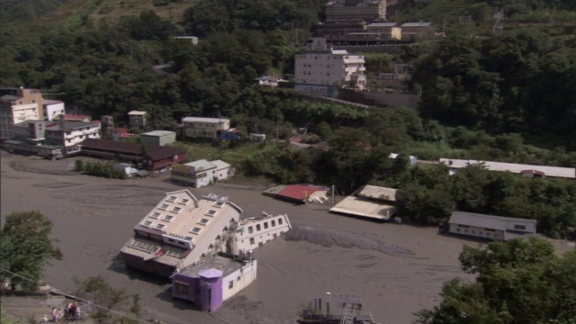 在一个山城的街道中央，一座建筑物侧卧在深深的泥浆中。视频素材