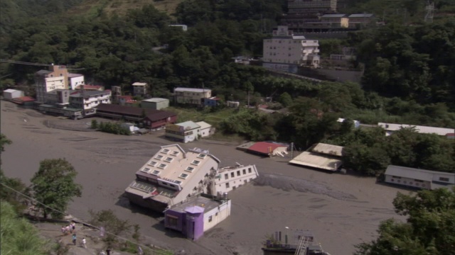 在一个山城的街道中央，一座建筑物侧卧在深深的泥浆中。视频素材