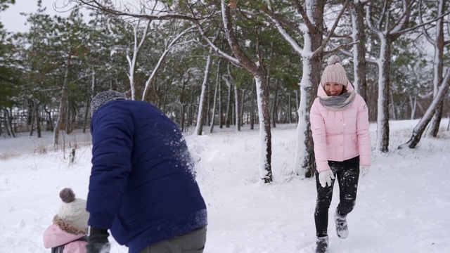 爸爸、妈妈、儿子和小女儿在雪天的树林里玩雪球。友好时尚的家庭在森林里扔雪的乐趣。人们一起享受寒假。慢动作视频素材