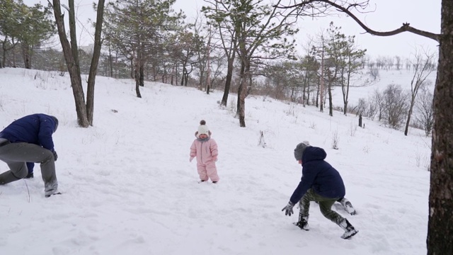 爸爸、妈妈、儿子和小女儿在雪天的树林里玩雪球。友好时尚的家庭在森林里扔雪的乐趣。人们一起享受寒假。慢动作视频素材