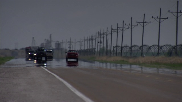 车辆行驶在被雨水打湿的道路上，经过一排电线杆。视频素材