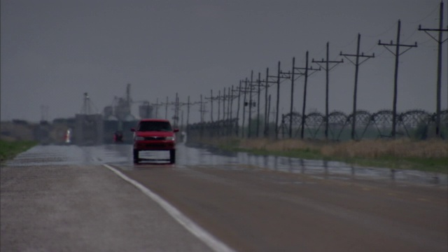 一辆汽车在被雨打湿的路上行驶，经过一排电线杆。视频素材