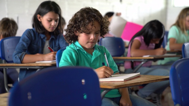 这个小男孩在课堂上和他的同学们一样专注于他的笔记本视频素材