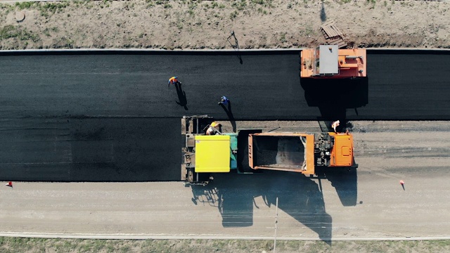 在俯视图中，沥青被铺在道路上。建筑工人正在修建道路。视频素材