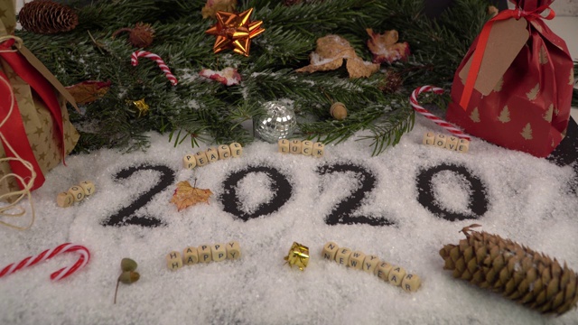 聚焦一个用雪写在前面的“2020”的安排，祝福平安、好运、爱情、快乐、新年快乐。背面装饰着冷杉、礼物和甘蔗视频下载