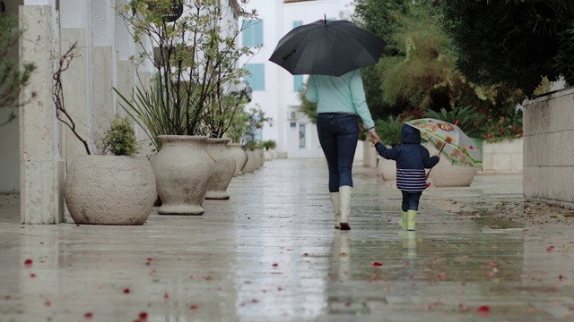 妈妈和她的儿子在雨中行走，穿着胶靴和雨伞。视频素材