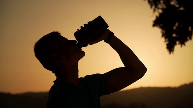 一个健康的年轻人在夕阳下喝水的剪影，分辨率为4k视频素材