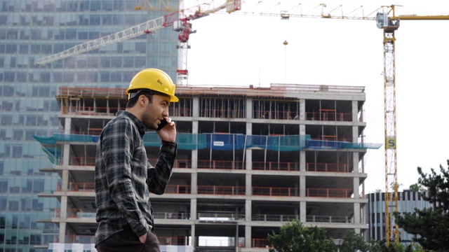 在建筑工地，一名戴着安全帽的工程师一边走路一边打电话视频素材