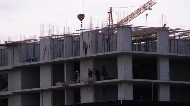 建筑工地上的建筑工人们。建筑工地上的起重机吊起重物。建筑施工视频素材