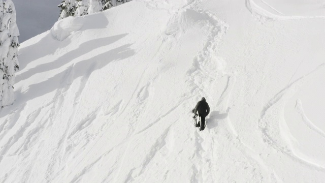 一个人徒步旅行与滑雪板攀登高山在滑雪胜地无人机空中角度视频素材