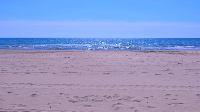 在阳光明媚的日子里，海滩上有蓝色的海水和泡沫状的波浪。视频素材