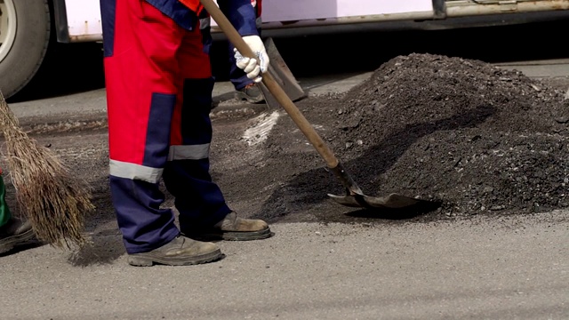 工人们用铁锹把旧的沥青从道路上铲下来，以便铺设新的沥青。视频素材