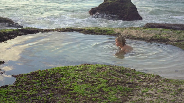 在巴厘岛的Pantai Tegal Wangi海滩上，一个小男孩在一个带有海水的天然小池塘里玩耍视频素材