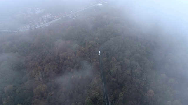 顶视图的白色卡车驾驶在危险，雾蒙蒙的森林道路。一架无人机在雾蒙蒙的道路上追赶一辆白色巴士视频素材