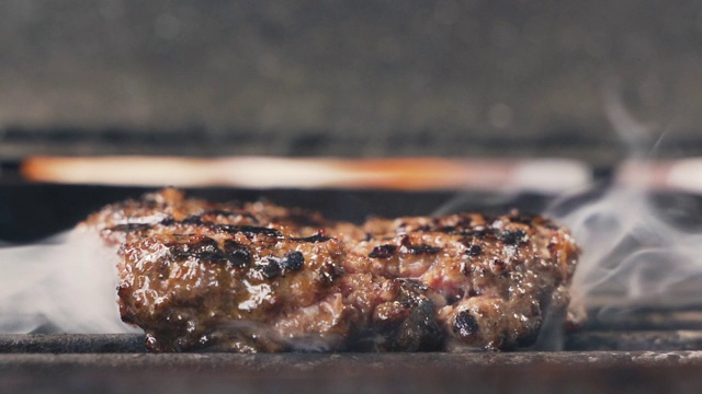 在炙热的烧烤架上烤出美味的汉堡肉。首席烹饪油近镜头不健康，但很满足蛋白质美味汉堡在休闲酒吧的慢镜头视频素材