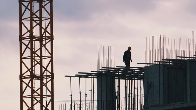 建筑工人在摩天大楼边缘的剪影。建筑工地的工人视频素材