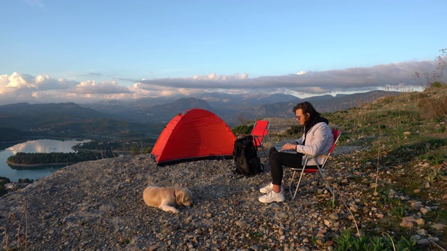 一个年轻人和她的狗在山顶上用笔记本电脑视频素材