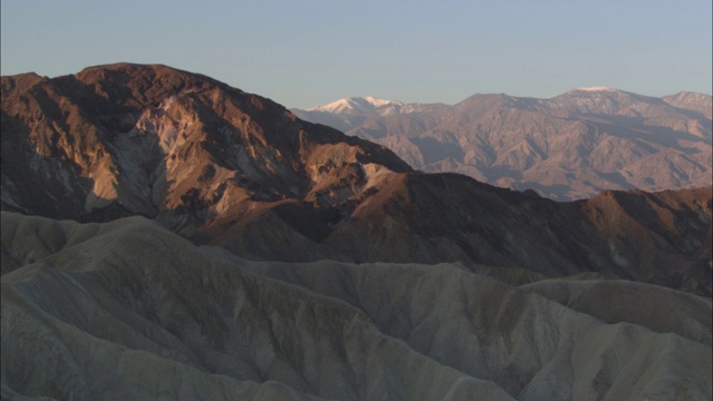 一座白雪覆盖的山峰坐落在死亡谷的沙漠山脉后面的地平线上。视频素材