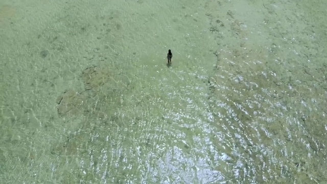 在菲律宾白色的沙滩和碧绿的海水中间，一架无人机从一名女子的头顶升起视频素材