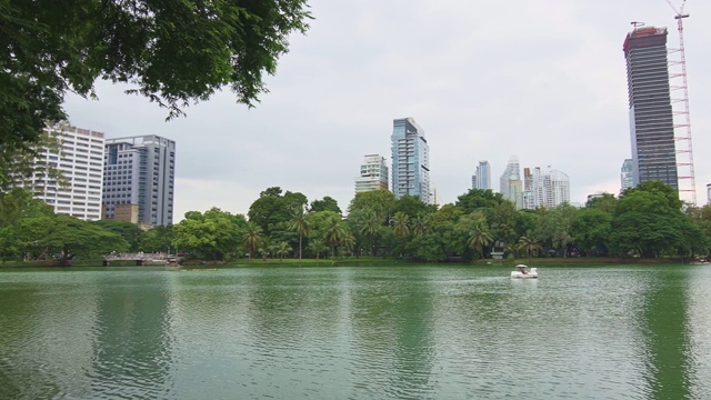 泰国曼谷隆皮尼中央公园。摩天大楼和现代未来建筑的城市全景。公园里的湖和天鹅游艇。倒影在水中。视频素材