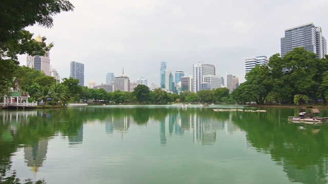 泰国曼谷隆皮尼中央公园。摩天大楼和现代未来建筑的城市全景。公园里的湖和天鹅游艇。倒影在水中。视频素材