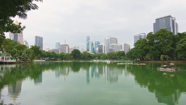 泰国曼谷隆皮尼中央公园。摩天大楼和现代未来建筑的城市全景。公园里的湖和天鹅游艇。倒影在水中。视频素材