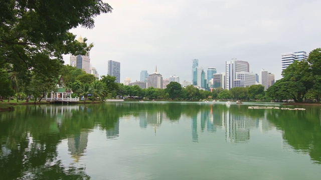 泰国曼谷隆皮尼中央公园。摩天大楼和现代未来建筑的城市全景。公园里的湖和天鹅游艇。倒影在水中。视频素材