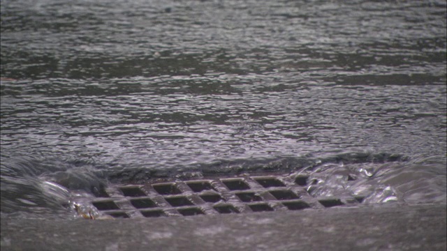 雨水沿着人行道流入街道上的金属格栅。视频素材