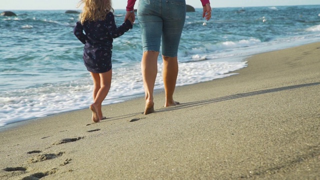 女人和女儿在海滩上散步的背影视频素材