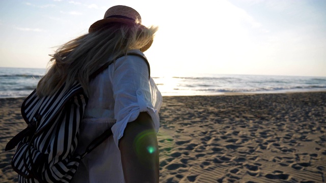 穿着沙滩装的女孩牵着男人的手，在夕阳下奔向大海。跟我拍的女人背包带领她的男朋友在海边。暑假或假期的概念。观点慢动作视频素材