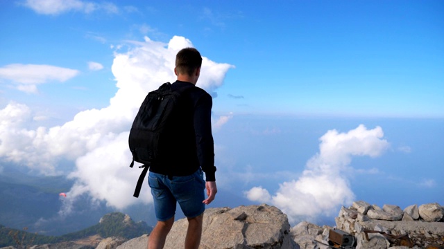 背包徒步者爬上边缘山，胜利地举起手。人在旅行中积极休息，在山顶享受自由。风景优美的景观作为背景。慢镜头视频素材