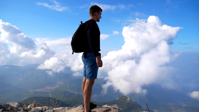 背包徒步者站在山边，胜利地举起手。人在旅行中积极休息，在山顶享受自由，欣赏风景。小车拍摄视频素材