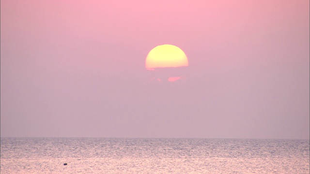 太阳在淡粉色的天空中在海面上落下。视频素材