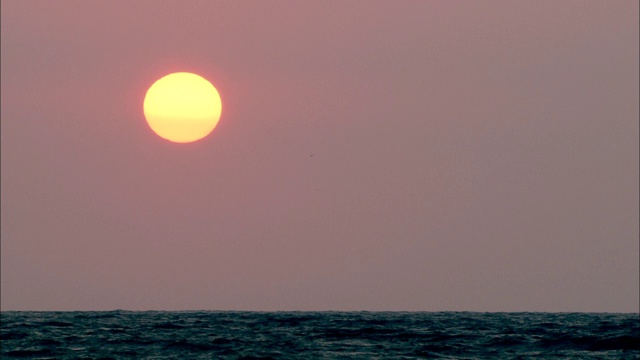 紫色的天空和橙色的太阳照耀着平静的海洋。视频素材