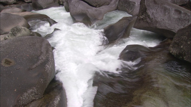 一条湍急的河流在顺流而下的途中冲过巨石。视频素材